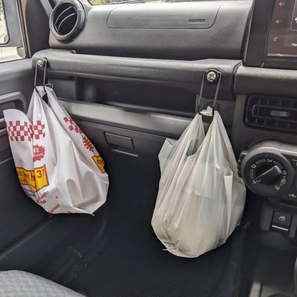 ARMORO JIMNY HOOKS WITH Two plastic bags hanging from hooks inside a vehicle's dashboard.